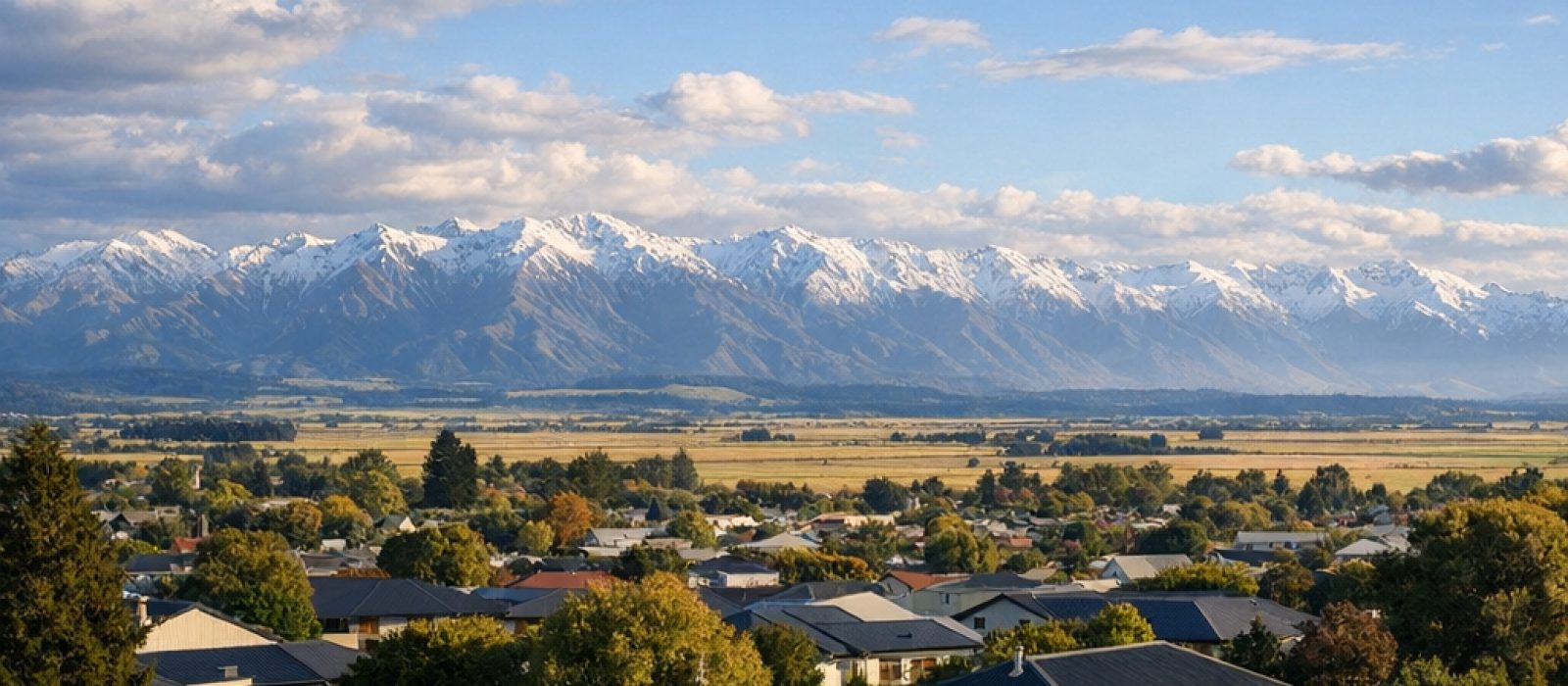 Long-run steel rooftops across a Canterbury town with the Southern Alps behind